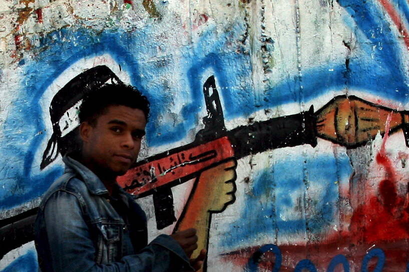 Palestyńczyk przechodzi na tle graffiti, przedstawiającego bojownika palestyńskiej organizacji Hamas z bronią, w Gazie w Strefie Gazy fot. PAP/EPA/Mohammed Saber