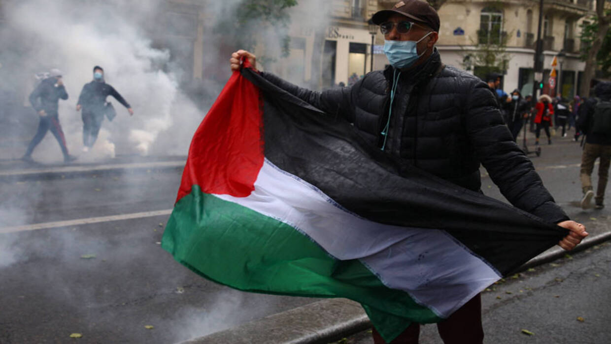  Mężczyzna trzyma flagę palestyńską, gdy protestujący stają twarzą w twarz z policją przeciwdziałającą zamieszkom podczas starć w ramach wiecu zorganizowanego przez kilka stowarzyszeń na rzecz ludności palestyńskiej w Paryżu. Fot. PAP/ EPA / CHRISTOPHE PETIT TESSON 